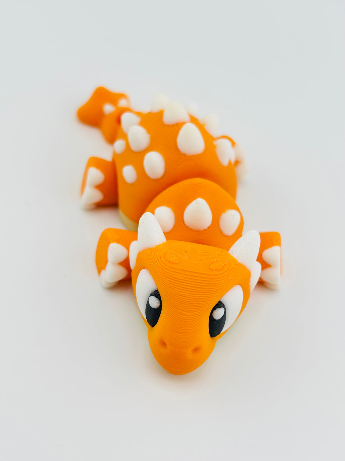 Orange baby ankylosaurus fidget toy with white spikes along its back