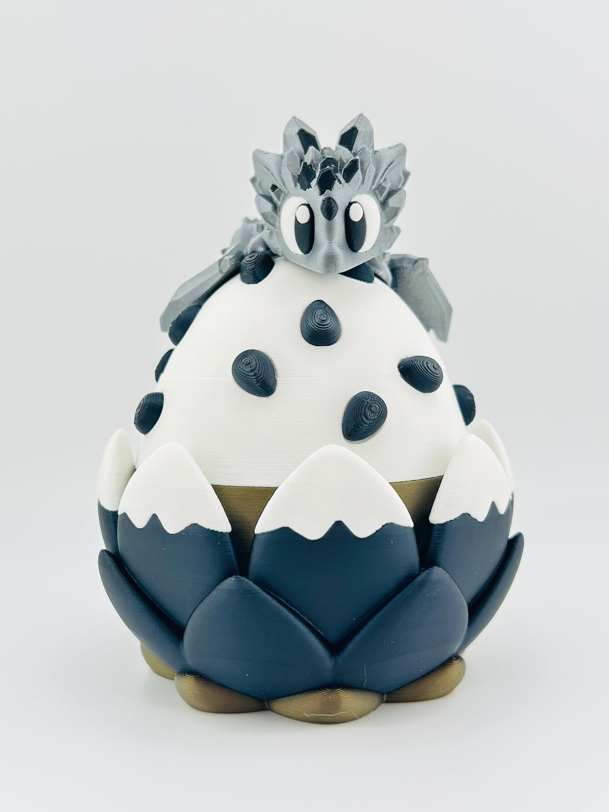 White and navy dragon egg with black spots and a small grey dragon perched on top