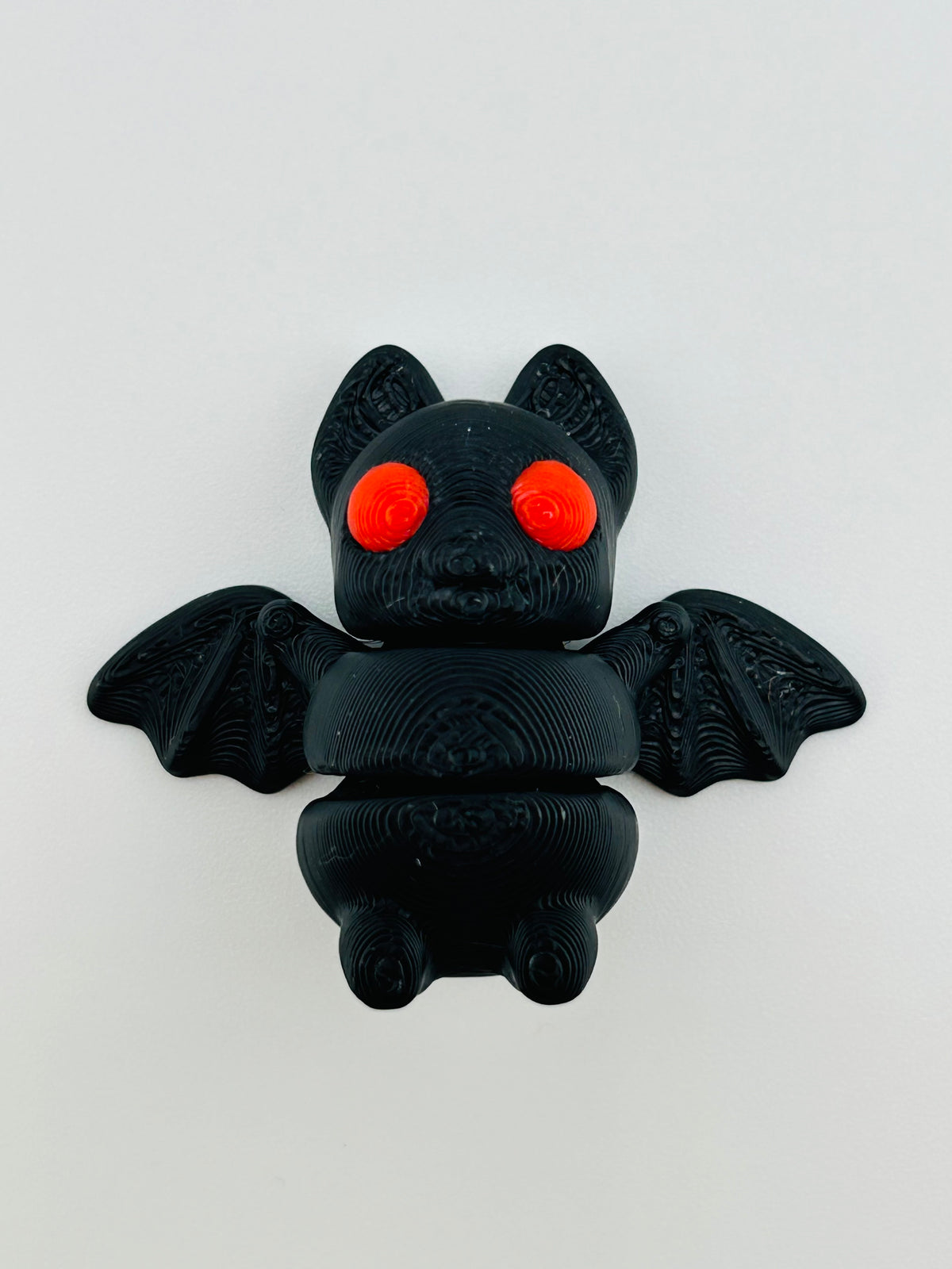 Black 3D printed bat fidget toy with red eyes and outstretched wings